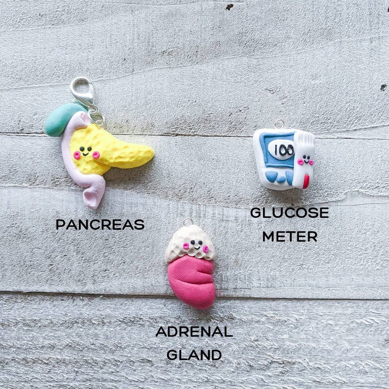 Three kawaii styled endocrinology charms – a yellow pancreas attached with duodenum and gallbladder, an adrenal gland on top of kidney, and glucose meter with a glucose strip.