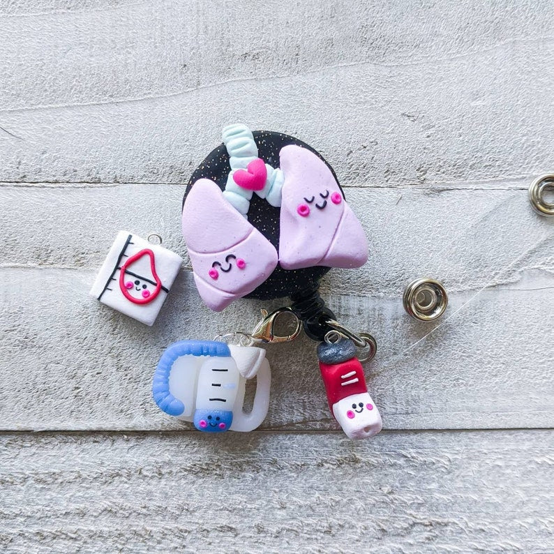 Pulmonary charms are shown being used as a badge reel accessory. There are 3 kawaii styled charms – a handheld blue spirometer, red albuterol inhaler, and pulmonary function test.