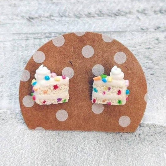 One pair of clay stud earrings. This pair is a sliced cake with rainbow sprinkles, white icing, and a dollop of swirled icing on top.